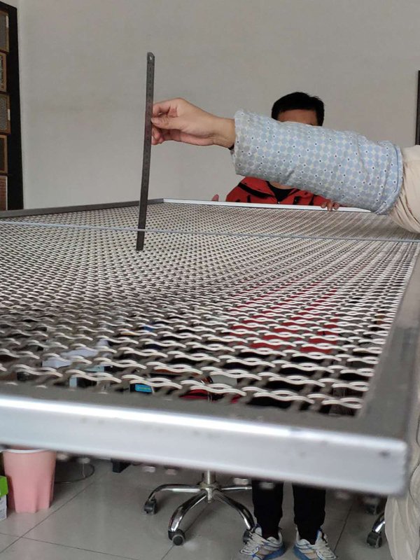 Inspecting a woven metal mesh panel with a steel rule in the Gecho workshop